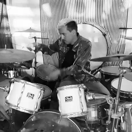 Black and white: a drummer mid-fill behind a kit, arms smeared with motion blur, cymbals caught in the swing.
