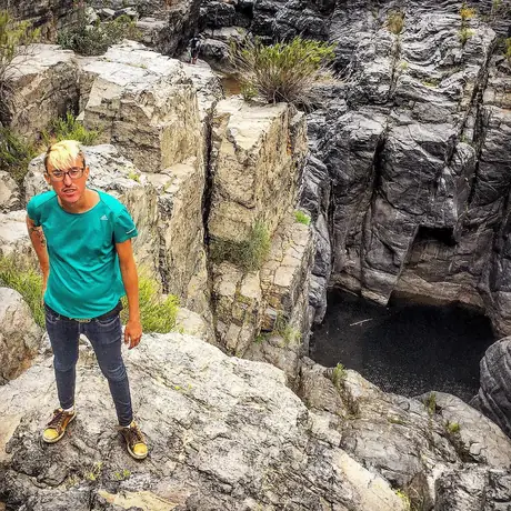 A figure in a teal shirt stands at the bottom of a narrow rock gully, pale grey boulders rising on both sides.